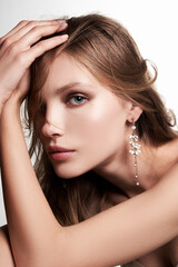 Naklejka premium Portrait of a dark blond lady with gentle makeup. The attractive girl is wearing golden clip-on earrings with pendants made as white flowers and beads and posing on the light background.