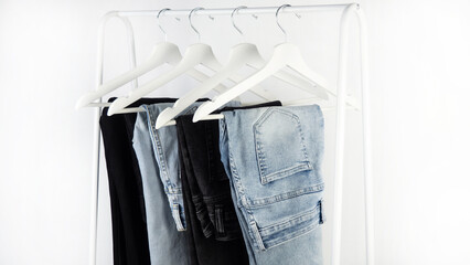 Different jeans hang on white clothes hangers. Casual jeans in a locker room on a white background.