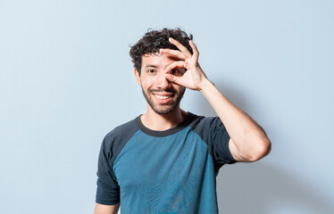 Friendly guy making ok gesture looking through fingers. Happy young man making ok gesture with hand looking through fingers. Teenage guy making ok gesture looking through fingers