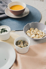 Top view of bowl with pumpkin seeds. On the background are pumpkin cream soup and crackers in blur. Near pumpkin seeds in a bowl is sour cream in bowl. 