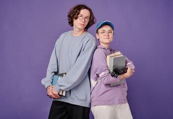 Portrait of couple of students in eyeglasses smiling at camera holding books against purple background