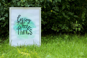 Poster with phrase Enjoy The Little Things on grass outdoors, space for text