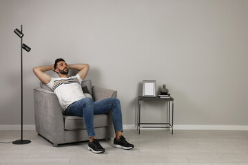 Man napping in armchair near gray wall, space for text