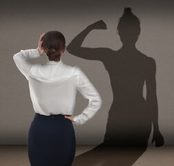 Businesswoman and shadow of strong muscular lady in front of her on grey wall. Concept of inner...
