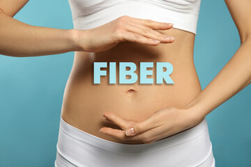 Woman holding hands near belly and word Fiber, closeup