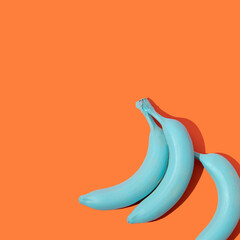 Creative layout with pastel blue bananas on bright orange background. 80s, 90s retro aesthetic style romantic concept. Minimal fashion surreal fruit idea.