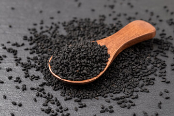 Black cumin seeds in a wooden spoon over black background. Nigella sativa for Ayurveda and herbal...