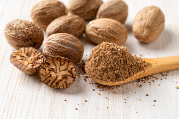 Spoon of ground nutmeg, whole and halved seeds over white wooden background. Muscat nuts closeup...