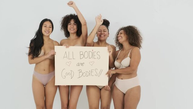 Happy diverse young ladies in lingerie showing placard with body positive inscription