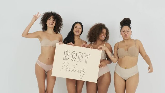 Smiling multiethnic fit and plus size women showing placard in studio