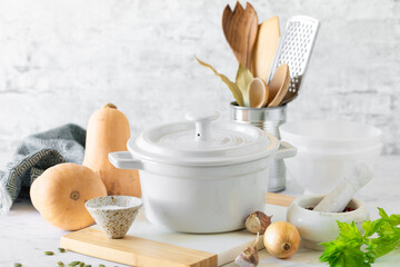White saucepan, kitchen utensils, ingredients for making fresh pumpkin soup on a white background. copy space