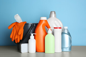 Different cleaning supplies and tools on wooden table against light blue background - Powered by Adobe