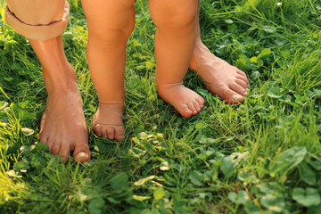 Woman with her child walking barefoot on green grass outdoors, closeup