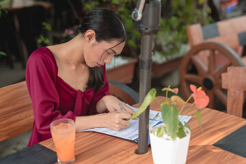 A busy trans woman signs documents as she works at and outdoor cafe.
