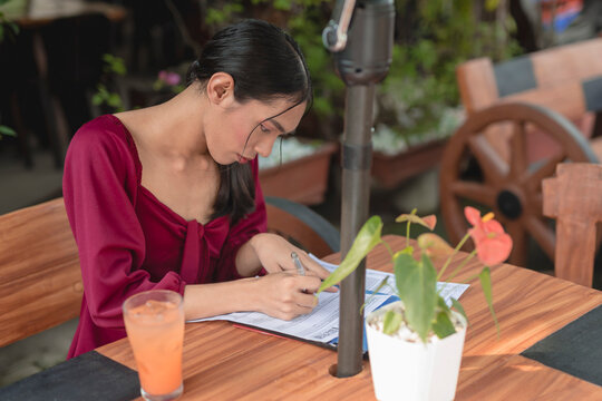 A Busy Trans Woman Signs Documents As She Works At And Outdoor Cafe.