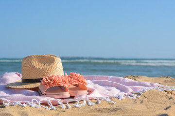 Blanket with stylish slippers and straw hat on sandy beach near sea. Space for text