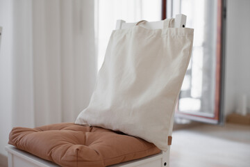 Linen tote bag mockup for inserting design.Medium size empty canvas mock up. Neutral beige bag at home lying on a chair at home in dining room at day time. Craft tote bag mockup in interior. 