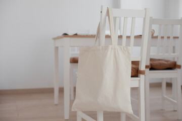 Fototapeta na wymiar Linen tote bag mockup for inserting design.Medium size empty canvas mock up. Neutral beige bag at home hanging on a chair at home in dining room at day time. Craft tote bag mockup in interior. 