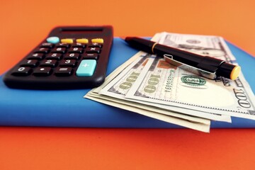 Black calculator, dollars cash money, pen on open notebook, isolated on orange background. Concept...