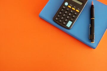 Black calculator, dollars cash money, pen on blue notebook isolated on copy space orange background. Concept of financial planning - money management or start business