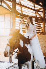 A charming boho bride rides a horse on a ranch at sunset in winter.