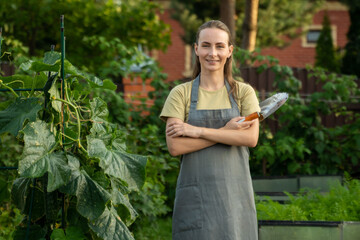 Woman holding a shovel in her arms crossed over her chest poses for a portrait in her garden. 