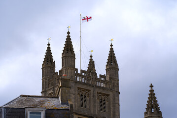 Tower with flag of famous Abbey Church of Saint Peter and Saint Paul at City of Bath on a blue cloudy summer day. Photo taken August 2nd, 2022, Bath, United Kingdom.