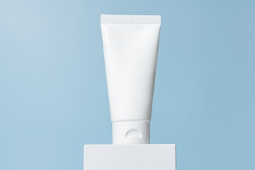 White cosmetic tube mockup. Plastic packaging for cosmetology cream product on a white podium on blue background. Skincare concept