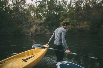 Man carrying kayak across river 