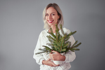 Happy young woman holding bouquet of pine tree branch against grey background.