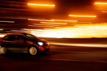 Obraz premium compact car at speed on the street with nighttime light trails
