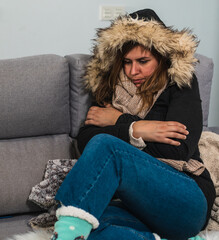 girl on the sofa at home wearing a coat and being cold