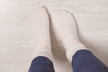 Women's feet in knitted, woolen white socks at home on a light floor. Cold floor in the apartment.Top view