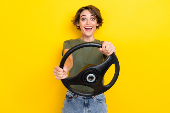 Photo Of Speechless Staring Open Mouth Girl With Bob Hairstyle Wear Khaki T-shirt Hold Steering Wheel Isolated On Yellow Color Background