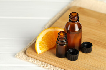 Bottles of essential oil and orange slice on white wooden table, closeup. Space for text