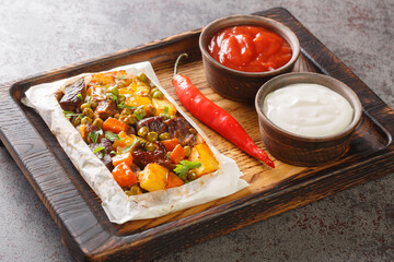 Turkish kebab with vegetables wrapped in parchment close-up on a wooden tray on the table. Horizontal