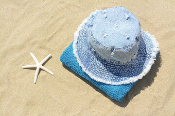Fototapeta na wymiar Stylish denim hat, towel and starfish on sand outdoors, above view. Beach accessories