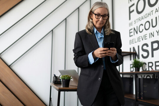 gray-haired Middle aged older business woman head by mobile phone in the office, concept of successful business development