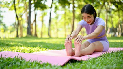 Naklejka na ściany i meble Healthy Asian woman in sportswear stretching her legs and arms on yoga mat