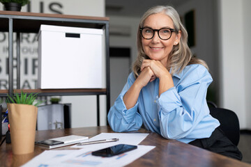 Successfully Middle aged older business woman head sits at a table and looks at the camera with her hands clasped in a lock, running a successful business Concept