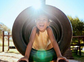 Child, smile and park on jungle gym, tyre and playing in sunshine, summer and outdoor while excited. Happy, girl and wow for laugh, happiness and playground in lens flare, comic and nature in Orlando © J Maas/peopleimages.com
