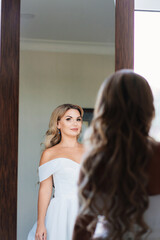 Fototapeta premium beautiful blonde bride in a white dress looks at the reflection in the mirror. 
