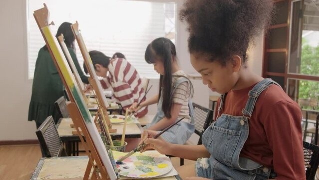 A group of multiracial kids learning with a female Asian teaches acrylic color picture painting on canvas in art classroom, creatively learning with skill at the elementary school studio education.