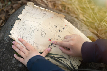 Pirate treasure map for kids.A family treasure hunting game. Outdoor games for the whole family. A treasure hunt quest. The child's hand points to the place with the treasure.