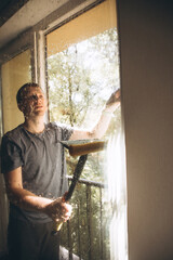 The man washes the windows at home using a window mop, cleaning the house. Front view, selective focus