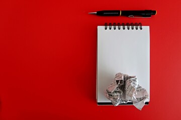 Notebook, pen and crumpled paper on red copy space background - Concept of first time writing, writers block, freelance writer or creative writing pieces project
