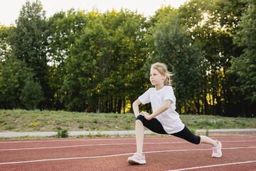 Obraz premium Child girl warming up on the sports track before running