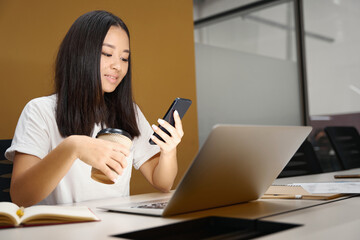 Charming business analyst with smart phone is reading message in modern office