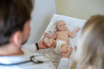 Cute baby lying on kids table while being examined by pediatrician