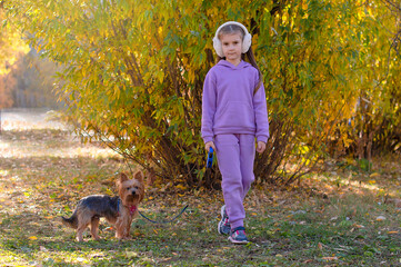 A smiling girl with her dog in the autumn park during a walk. A little girl hugs a puppy sitting on a bench, Best friends. Selective focus